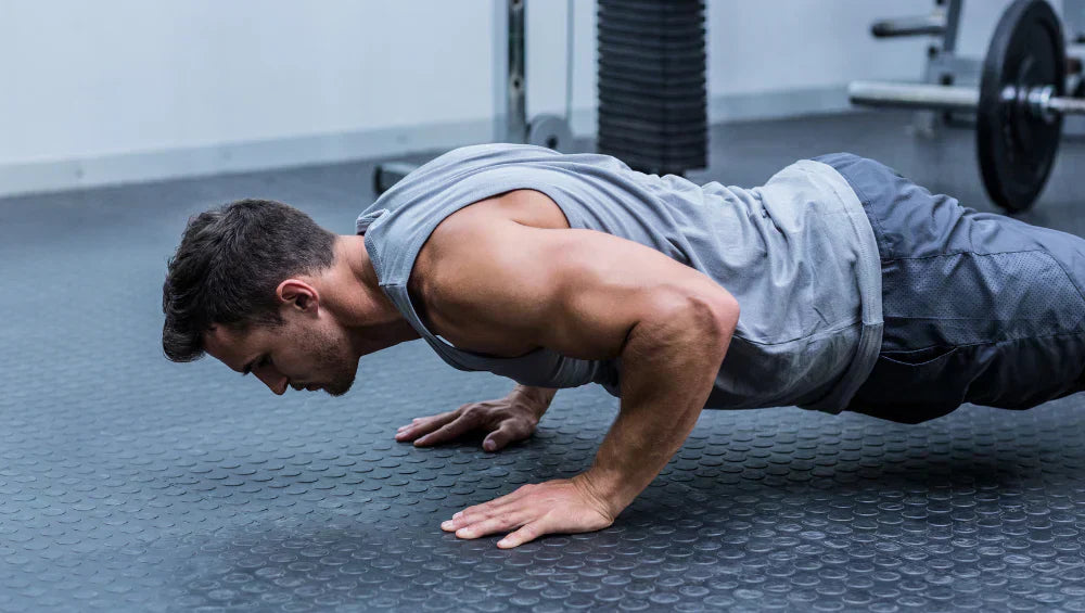 Homme musclé en débardeur gris dans une salle de gym grise en train d'effectuer une série de pompe