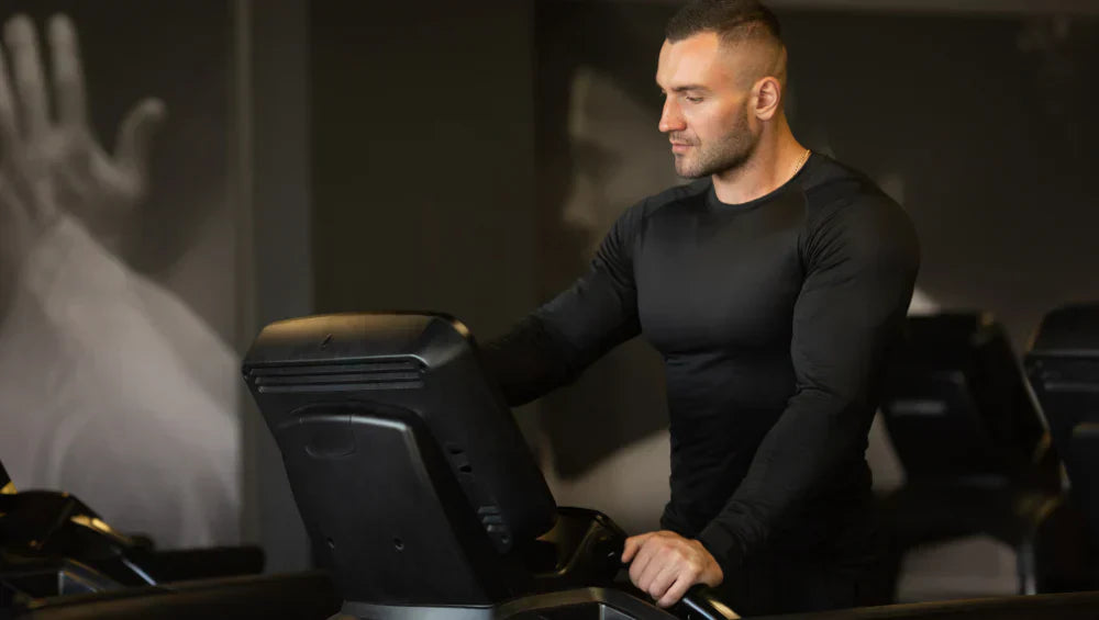 Homme en tenue de sport dans une salle de gym en train de choisir un programme sur une machine tapis roulant