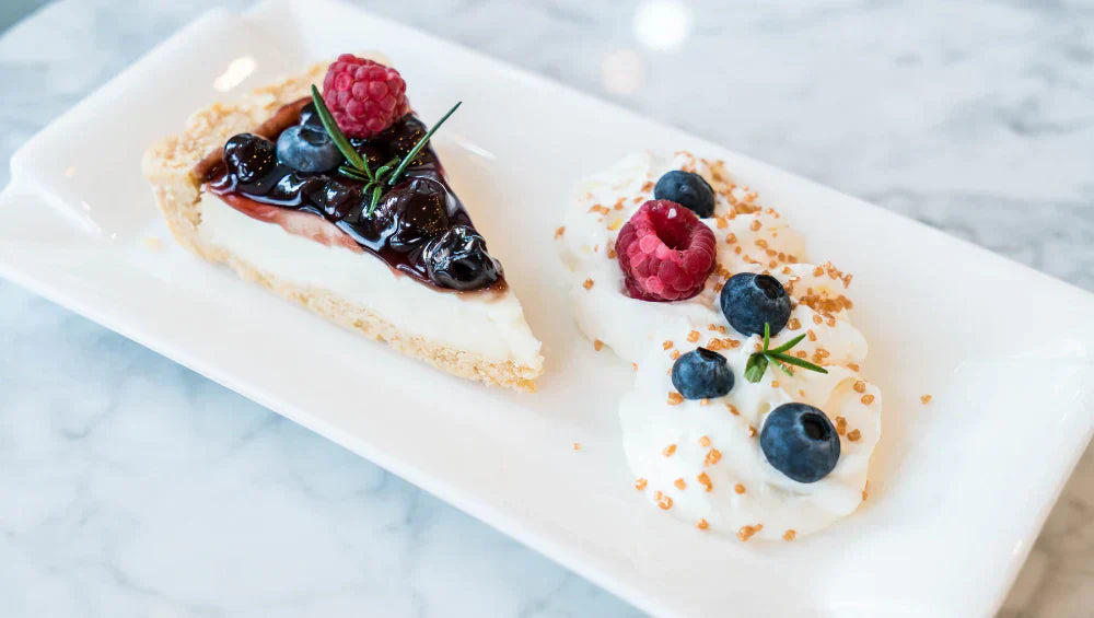 Cheesecake protéiné sur une assiette blanche rectangulaire acompagné de crème et fruits des bois