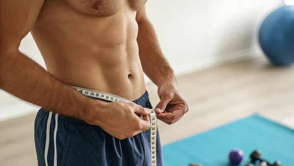 Homme sec et muscle torse nu dans une salle de sport en train de prendre ses mensuration au niveau de la taille