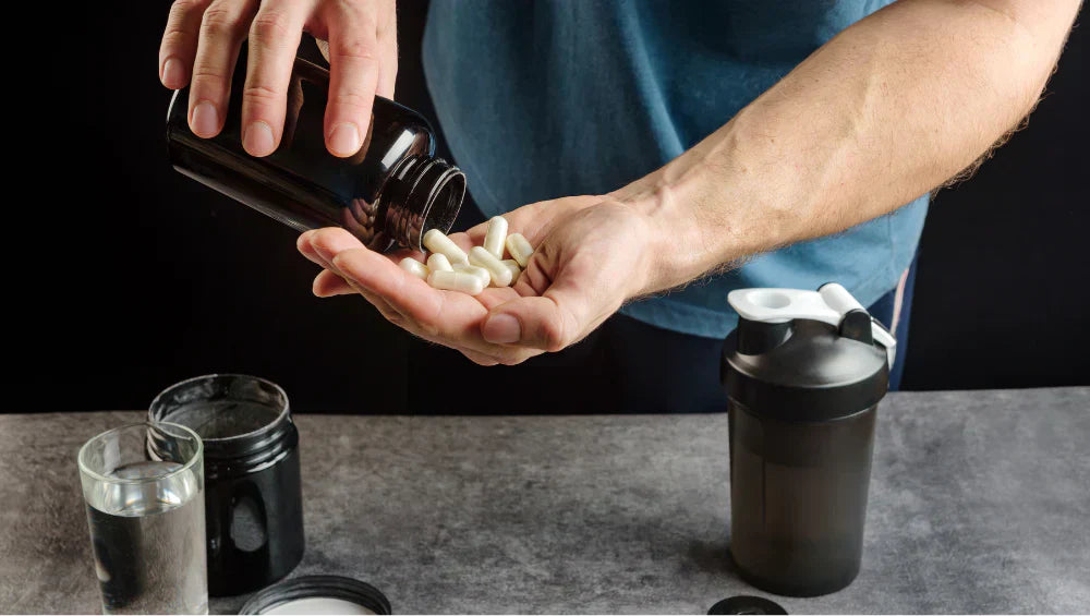 Homme en train de prendre des pilules blanche (fat burner) dans ça main, devant lui un shaker, un pot de glutamine et un verre d'eau