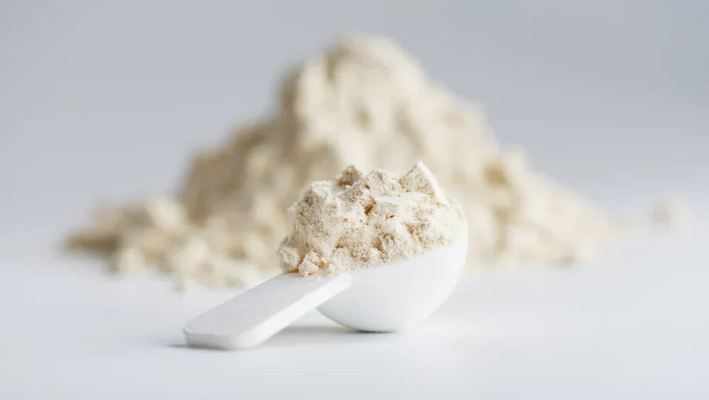 Une scoop remplis de creme de riz sur un fond blanc avec en arrière plan un tas de poudre blanche