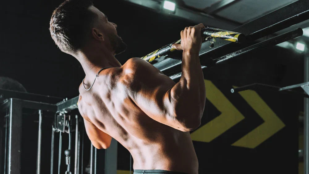 Homme musclé torse nu en train d'effectuer une série de traction pronation dans une salle de gym