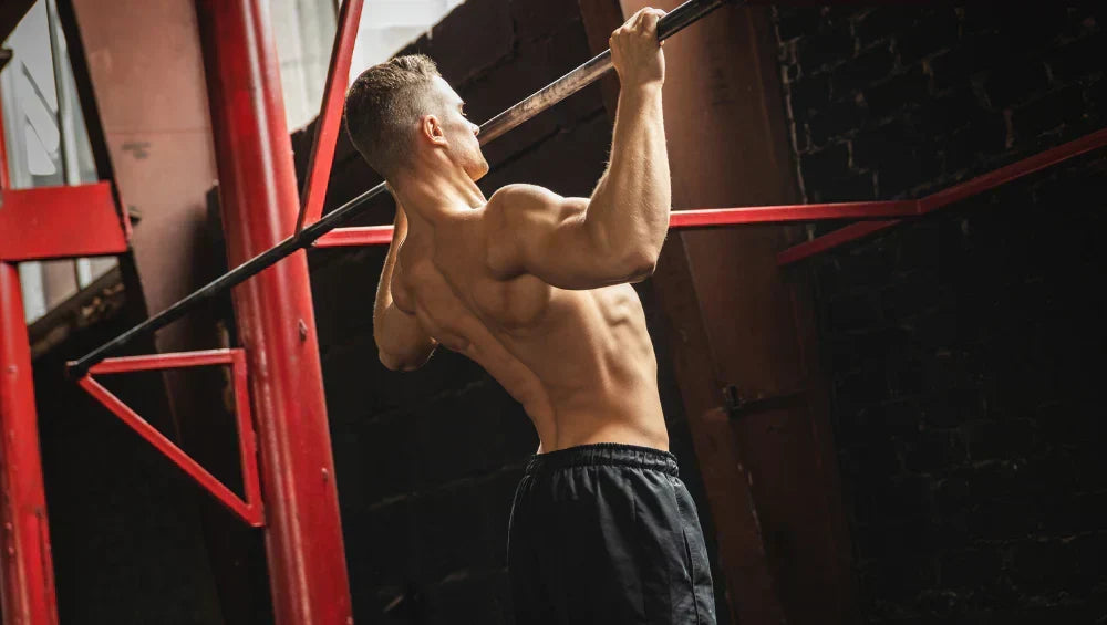 Homme sec et musclé en train d'effectué une série de traction sur une barre dans un gymnase façon old school