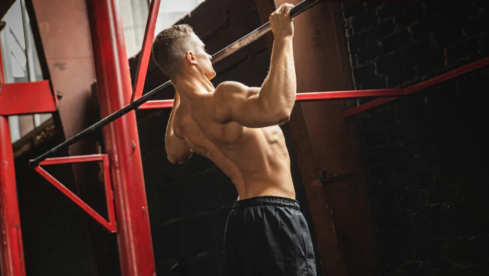 Homme sec et musclé en train d'effectué une série de traction sur une barre dans un gymnase façon old school