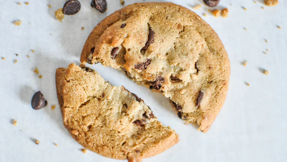 Cookie protéiné vu du haut sur une table blanche entourée de miette et de pépite de chocolat