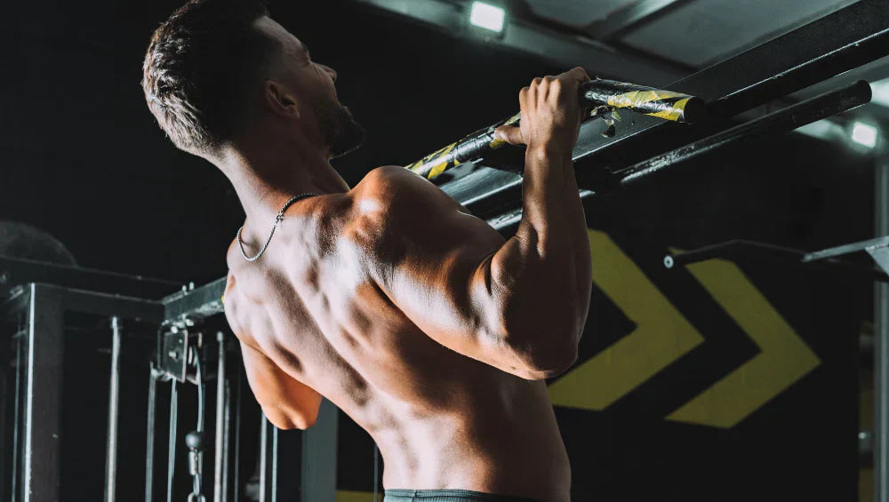 Homme musclé torse nu en train d'effectuer une série de traction pronation dans une salle de gym