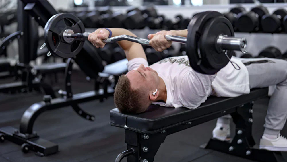 Homme allongé sur un banc en train de faire de la barre EZ au front