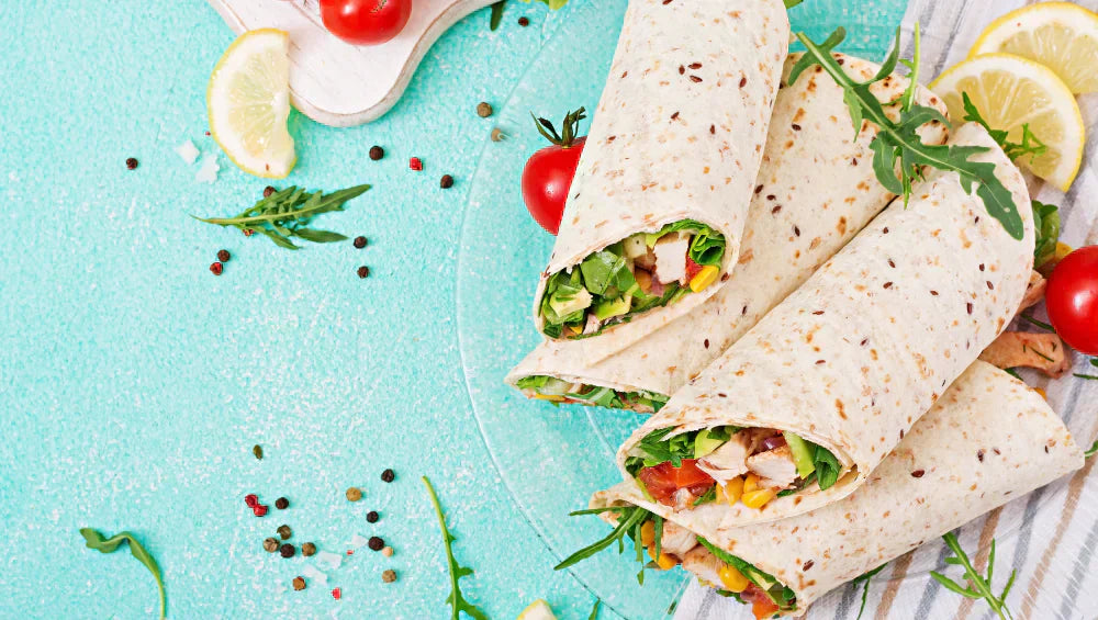 Plusieurs wrap au poulet avec des crudités réparti sur une table bleu